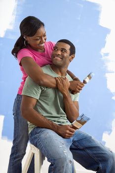 Portrait of African American male and female couple next to half-painted wall.