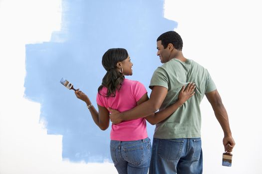 African American couple standing together looking at half-painted wall.