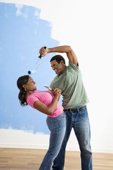 African American young man pretending to paint woman's face with paint roller.