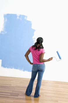 African American young woman standing next to half-painted wall with paint roller.