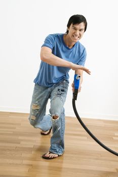 Asian young man aiming gasoline pump nozzle like a gun.