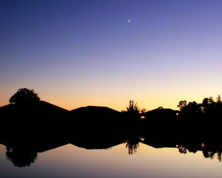 A sunset over a lake with silhouettes and reflections of the houses on the other side.