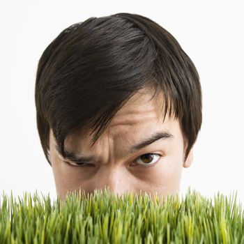 Asian young man looking over grass with eyebrow cocked.
