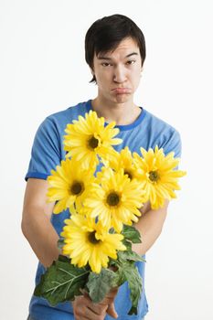 Asian young man holding bouquet of yellow gerber daisies with pout on his face.