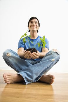 Asian man sitting holding growing cayenne plant.