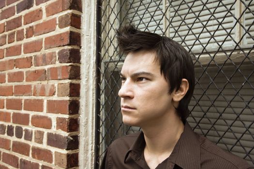 Asian man leaning against window near brick wall.