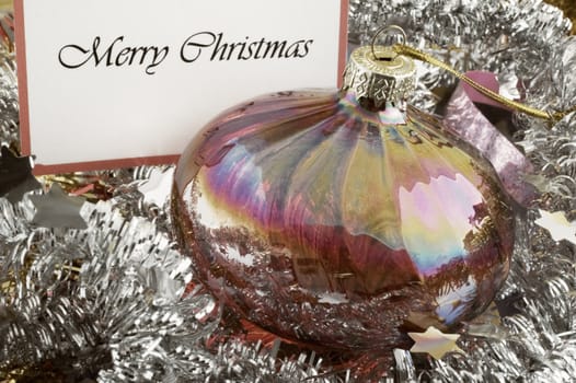 Retro looking glass Christmas bauble among tinsels with Merry Christmas card