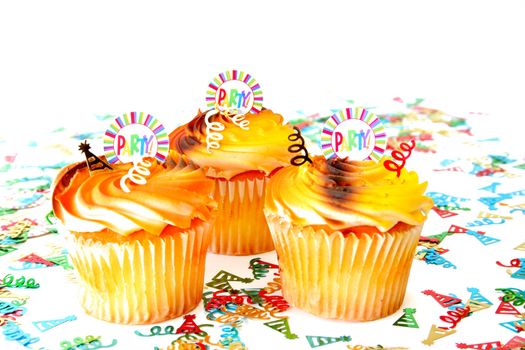 Three cupcakes with confetti all on a white background.  The cupcakes have a decoration with the word party on them. Used a shallow depth of field and selective focus.