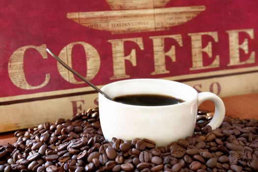 Cup of coffee surrounded by coffee beans and a handmade sign with the word coffee in the background.