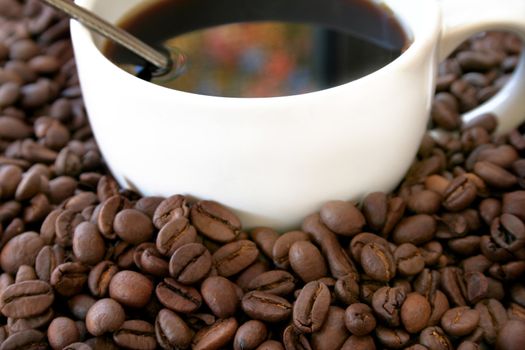 Close up of coffee beans and a cup of coffee with fall colors reflecting in the coffee.