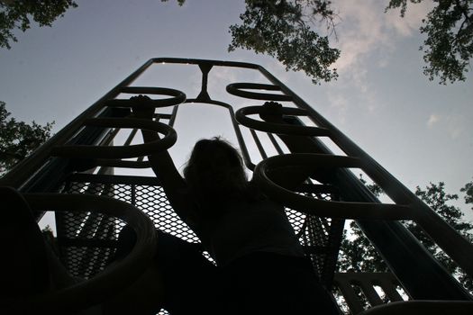 Silhoutte of Lucy climbing up a climbing frame.