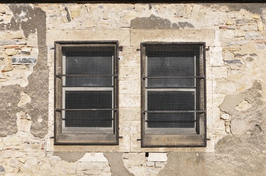 Two old windows with metallic grids on a clear stones wall