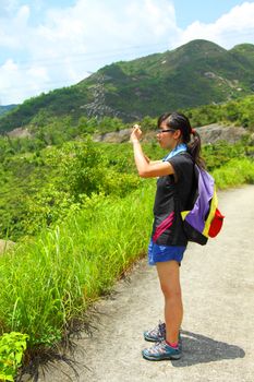 Young woman with backpack hiking and taking a photo 