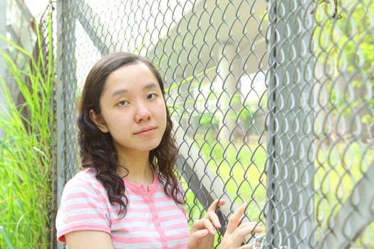 Asian girl with sad face, standing next to a net. She wants to escape from now's life. 