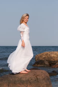 Beautiful woman in white dress standing on the rock and posing