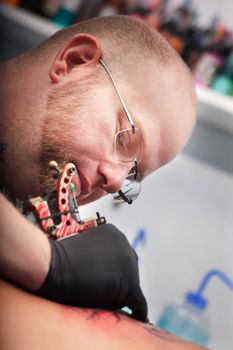 Caucasian tattoo artist draws tattoo on someone's back