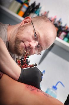 Bald Caucasian tattoo artist draws design on woman's back