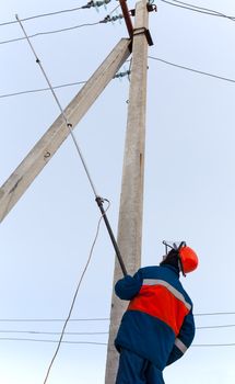 electrician in blue overalls establishes protective earth wire to the power line