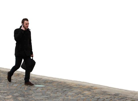 Businessman walking on a cobbled street in front of a white wall while using his mobile.