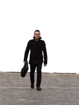 Young businessman walking through the camera on a cobbled street in front of a white wall.