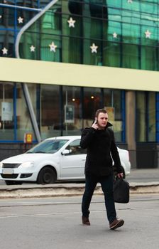 Young businessman on the phone crossing the street in an old European city.