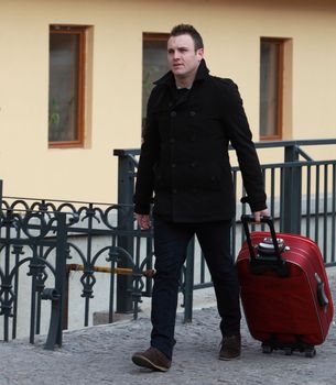 Young man with a red suitcase in a small cobbled street in a city.