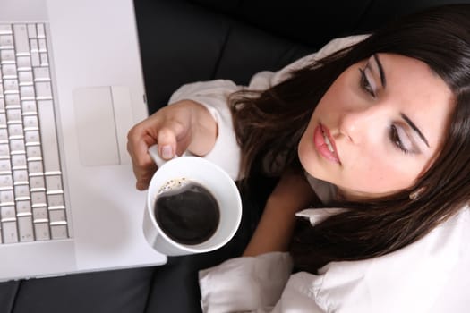 A young, hispanic adult girl watching a Laptop while drinking coffee.