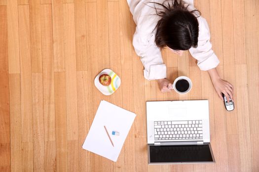 A young adult woman studying on the floor.
