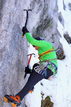 climber in action with two axes on a frozen waterfall