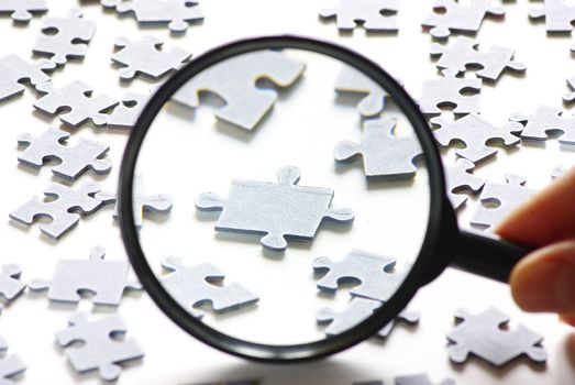 Hand with magnifying glass and puzzle isolated on white background