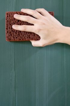 Female hand erasing a greenish chalkboard.