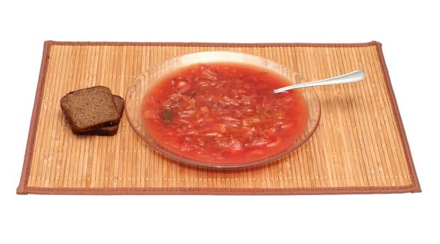 Plate with a borsch and rye bread on a bamboo mat.
