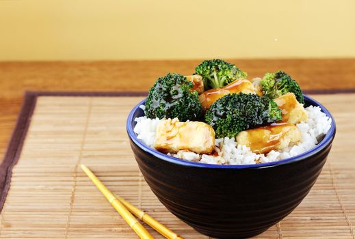 Vegetarian dish of stir fried tofu, broccoli and orange sauce with chopsticks. Selective focus on food with some blur on lower portion of image.

