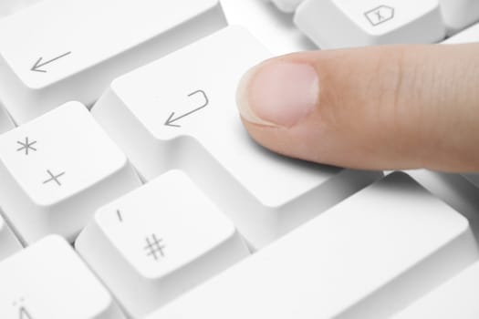 Forefinger pressing the "enter" button on a white keyboard.