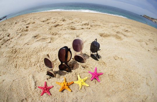 Holiday with friends � four pair of sunglasses on the beach and multi color sea stars
	