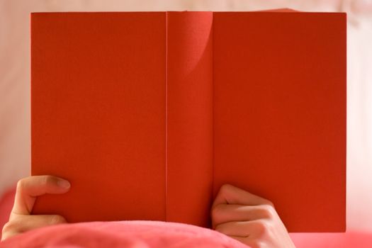 Person in bed reading in a red book.