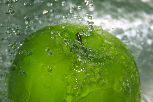 Water drops falling onto a green apple