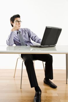 Asian businessman sitting at desk working on laptop computer.