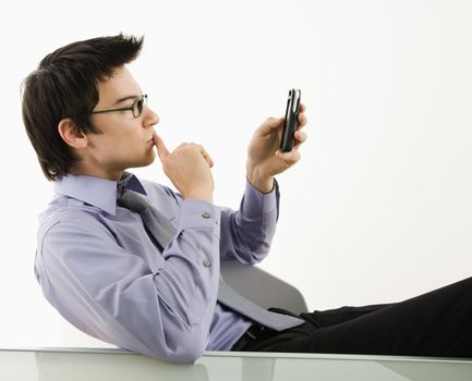 Asian businessman sitting at desk texting using his pda cellphone.