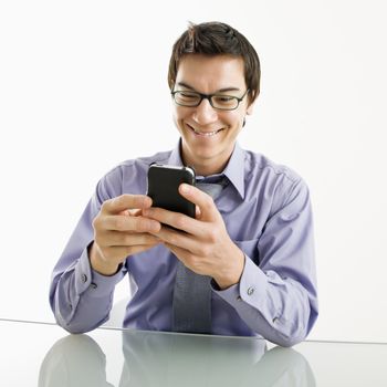 Smiling Asian businessman sitting at desk texting using his pda cellphone.