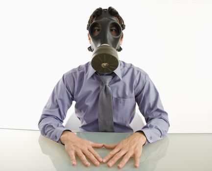 Businessman sitting in white room wearing gas mask.