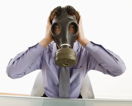 Businessman sitting wearing gas mask holding his hands over his ears.