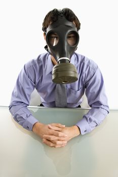 Businessman sitting in white room wearing gas mask.