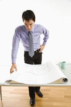 Asian business man standing looking over blueprints.