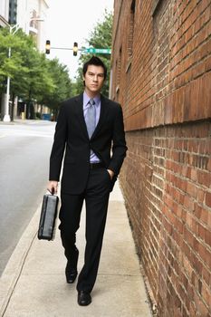 Asian business man walking down sidewalk in the city.