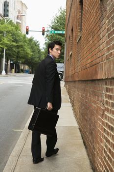 Asian business man walking down sidewalk in the city looking back at viewer.