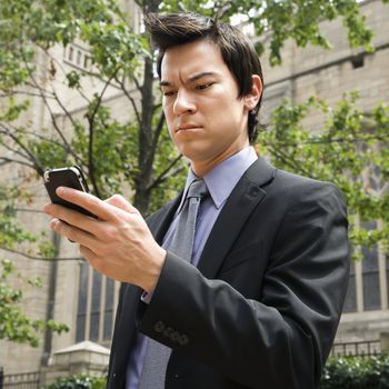 Asian business man standing looking at cell phone messages.