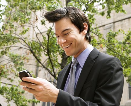 Asian business man standing looking at cell phone messages laughing.