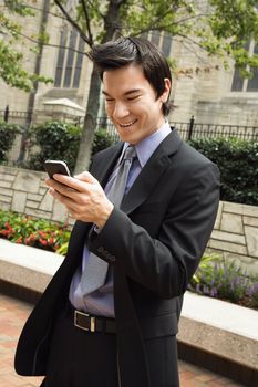 Asian business man standing looking at cell phone messages smiling.