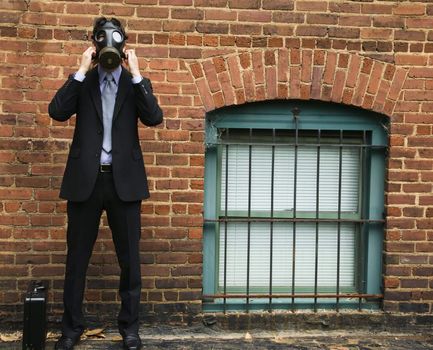 Businessman standing next to brick wall wearing gas mask.